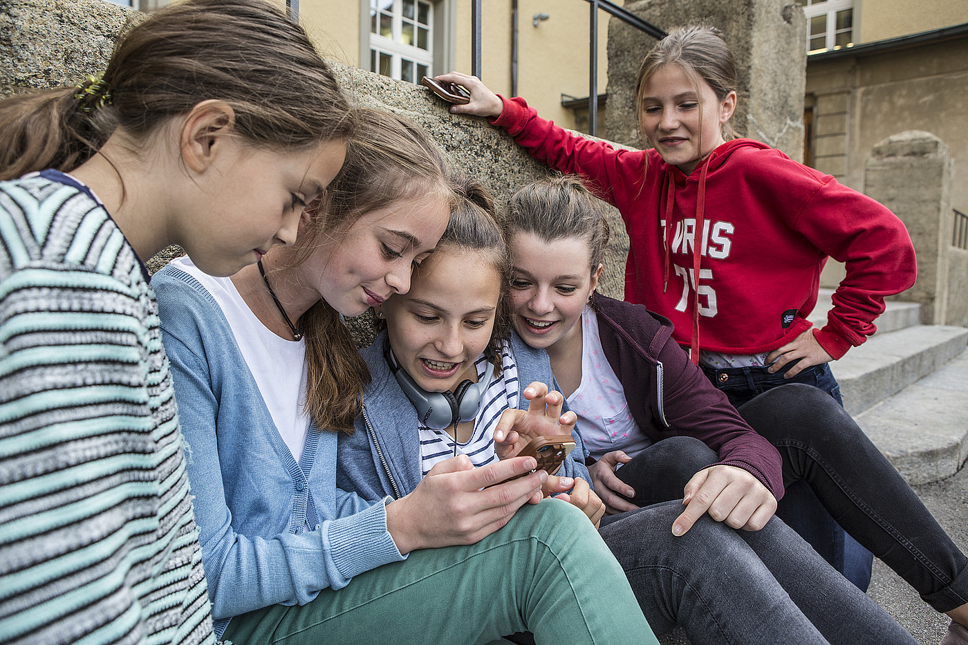 Cinq adolescentes regardent un téléphone portable à l'extérieur. 