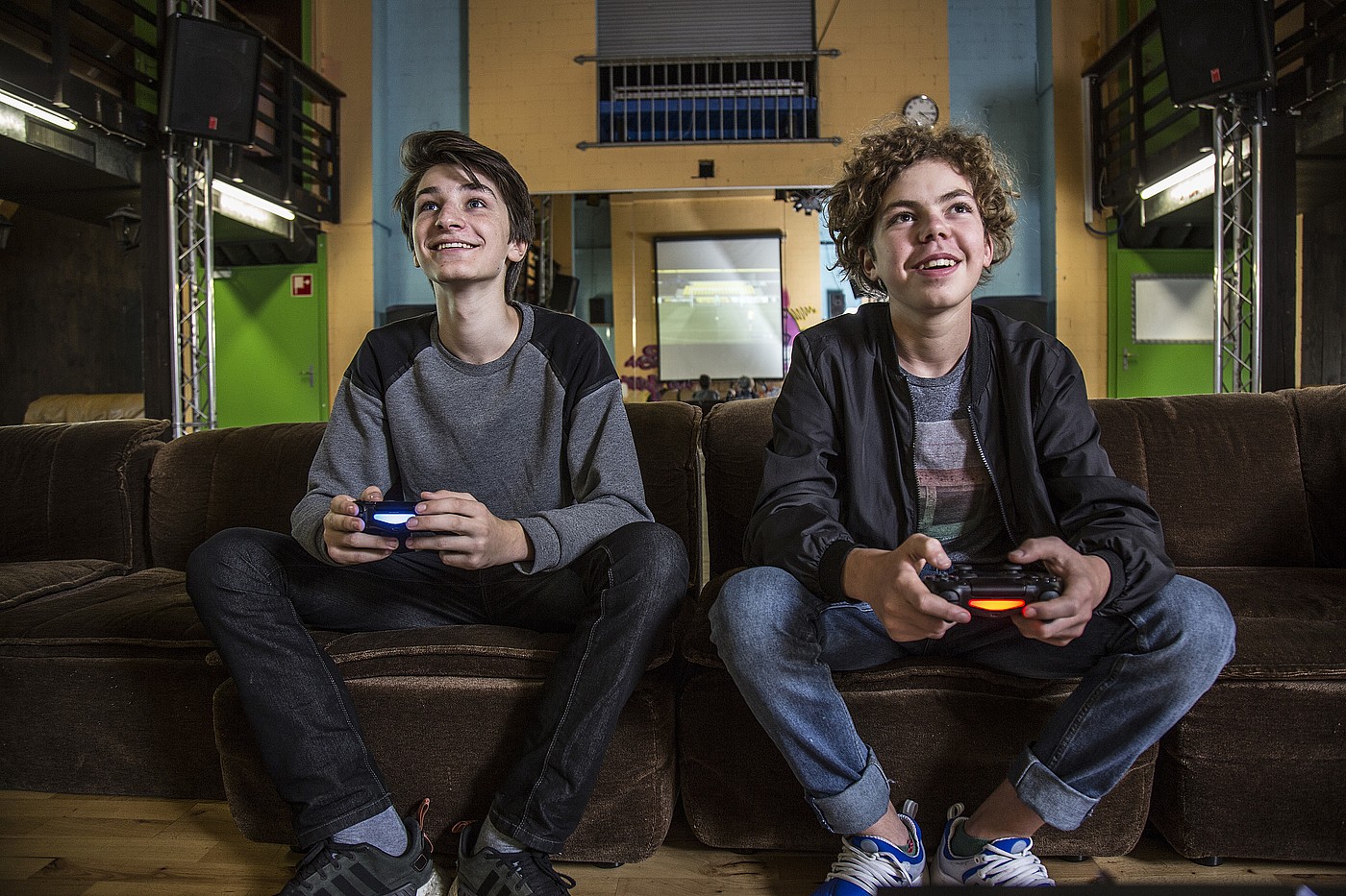 Deux adolescents assis sur un canapé dans un club de jeunes jouent ensemble à un jeu vidéo.