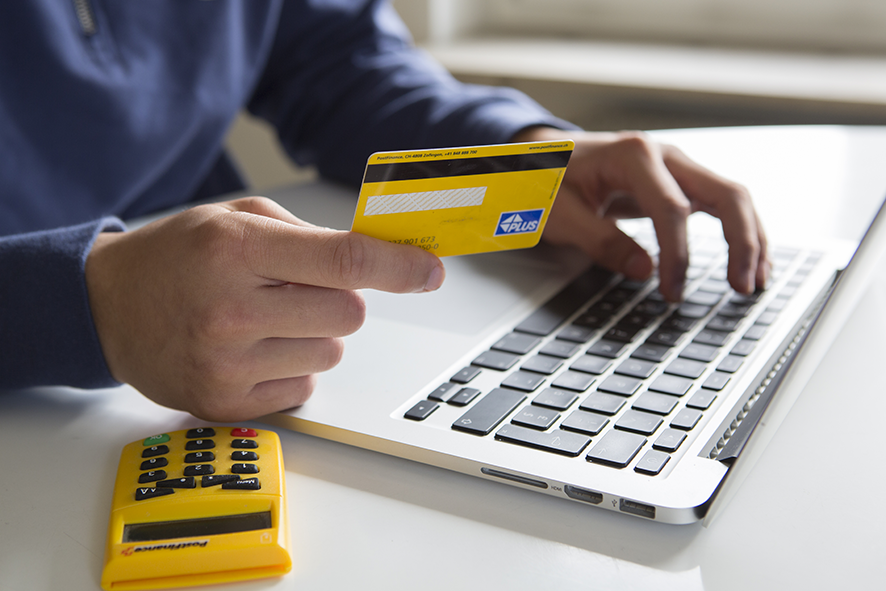 Une personne assise devant un ordinateur portable avec une carte bancaire en main.