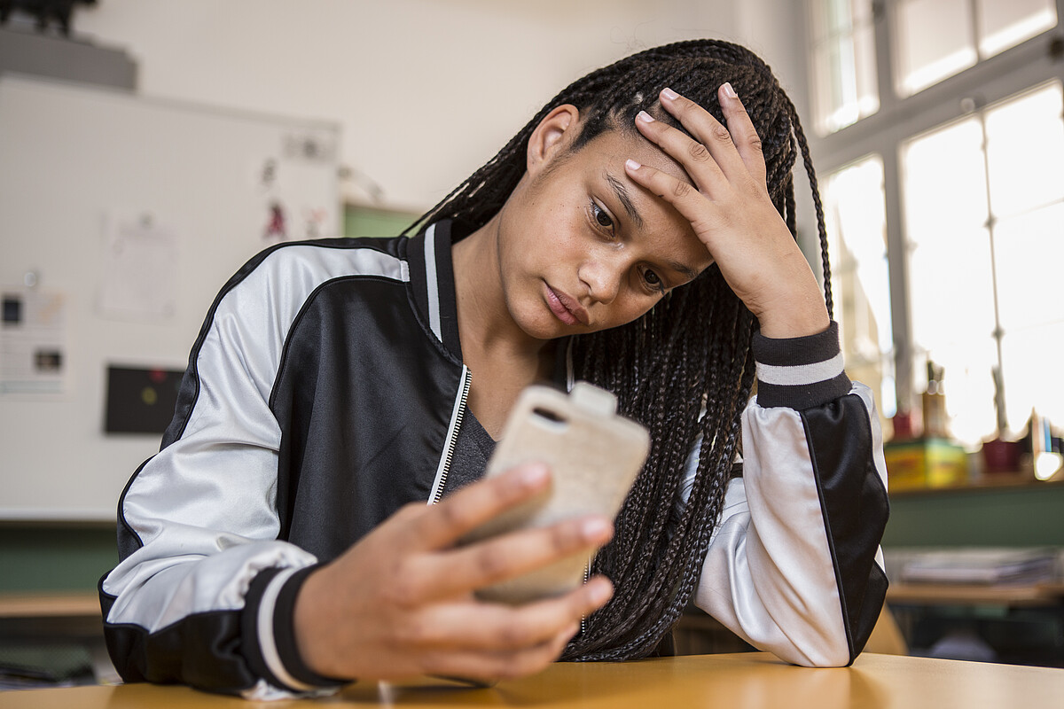 Une adolescente en détresse est assise sur son téléphone portable.