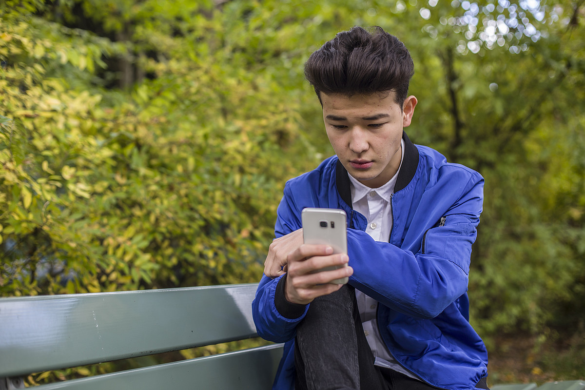 Un garçon est dehors et est sur son téléphone portable. Il porte une veste bleue.