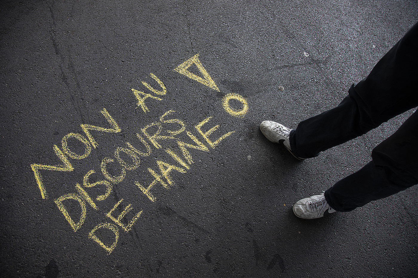 A côté des pieds d'une personne, "Non au discours de haine !" est écrit à la craie sur le sol.