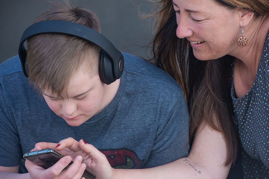 Une personne adulte montre quelque chose sur un smartphone à un jeune ayant des besoins particuliers.