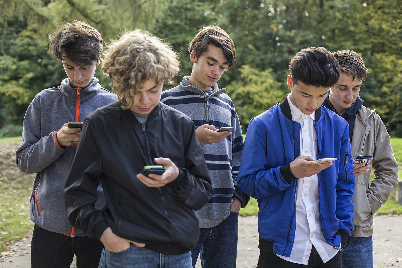 Cinq adolescents se tenant dehors et regardant tous leurs smartphones.