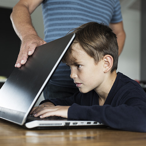 Un garçon est concentré sur l'écran et ne peut pas remettre l'ordinateur portable.