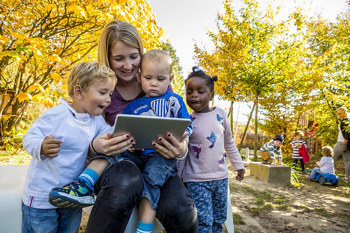 Une assistante maternelle regarde quelque chose avec les enfants sur la tablette.