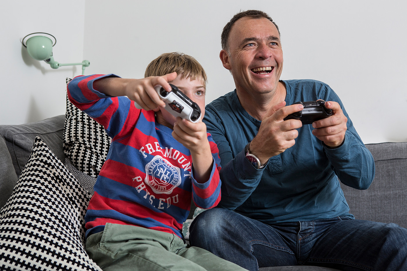 Un père assis sur le canapé avec son fils jouant à des jeux vidéo. 