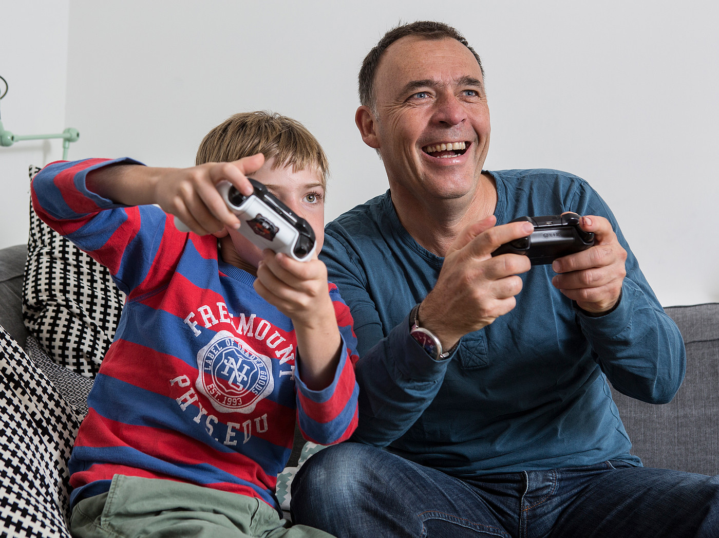 Un père assis sur le canapé avec son fils jouant à des jeux vidéo. 