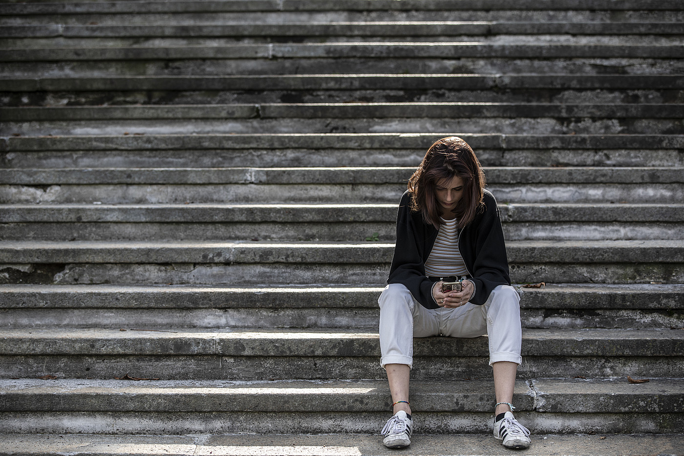 Une jeune femme assise seule dans un escalier consulte son smartphone. Représentation symbolique d'une situation de cybergrooming. Capture d'écran de la vidéo de la nouvelle campagne de Protection de l'Enfance Suisse contre la pédophilie. Infractions cybersexuelles