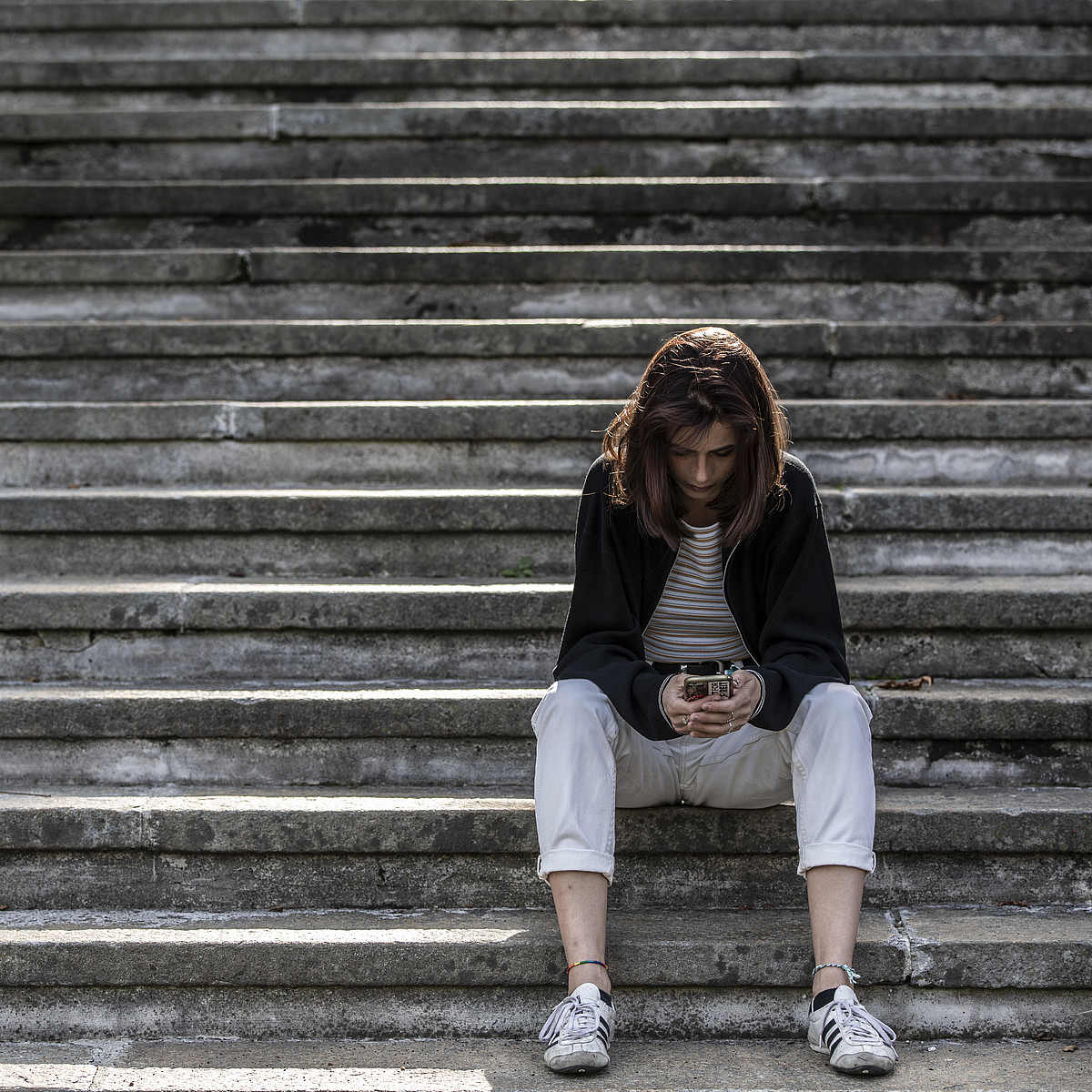 Une jeune femme assise seule dans un escalier consulte son smartphone
