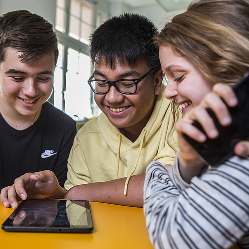 Des jeunes gens heureux utilisant leur téléphone portable en classe.