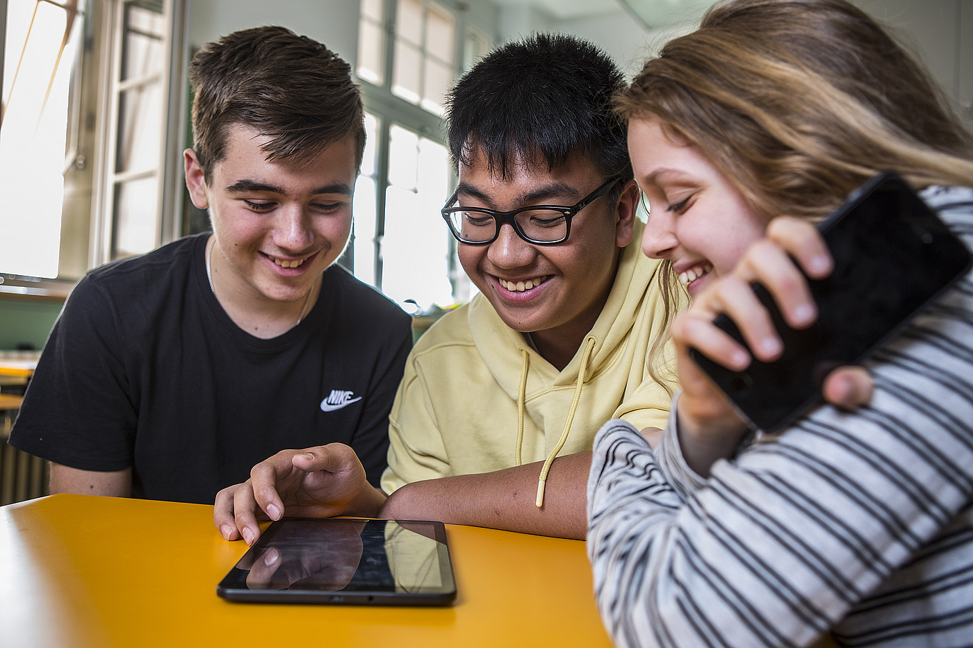 Des jeunes gens heureux utilisant leur téléphone portable en classe.