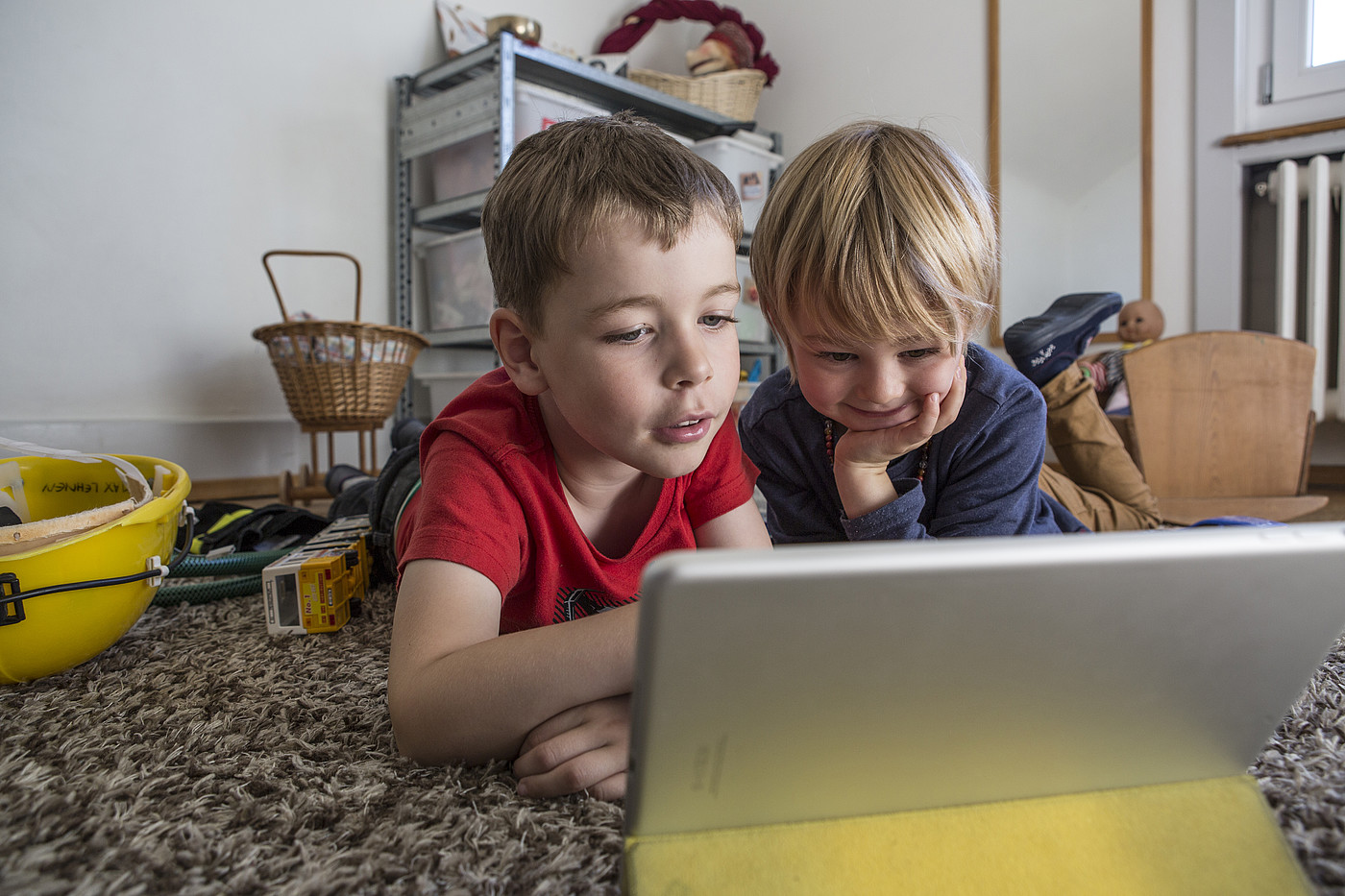Deux enfants allongés sur le sol dans une chambre d'enfant regardant une tablette.