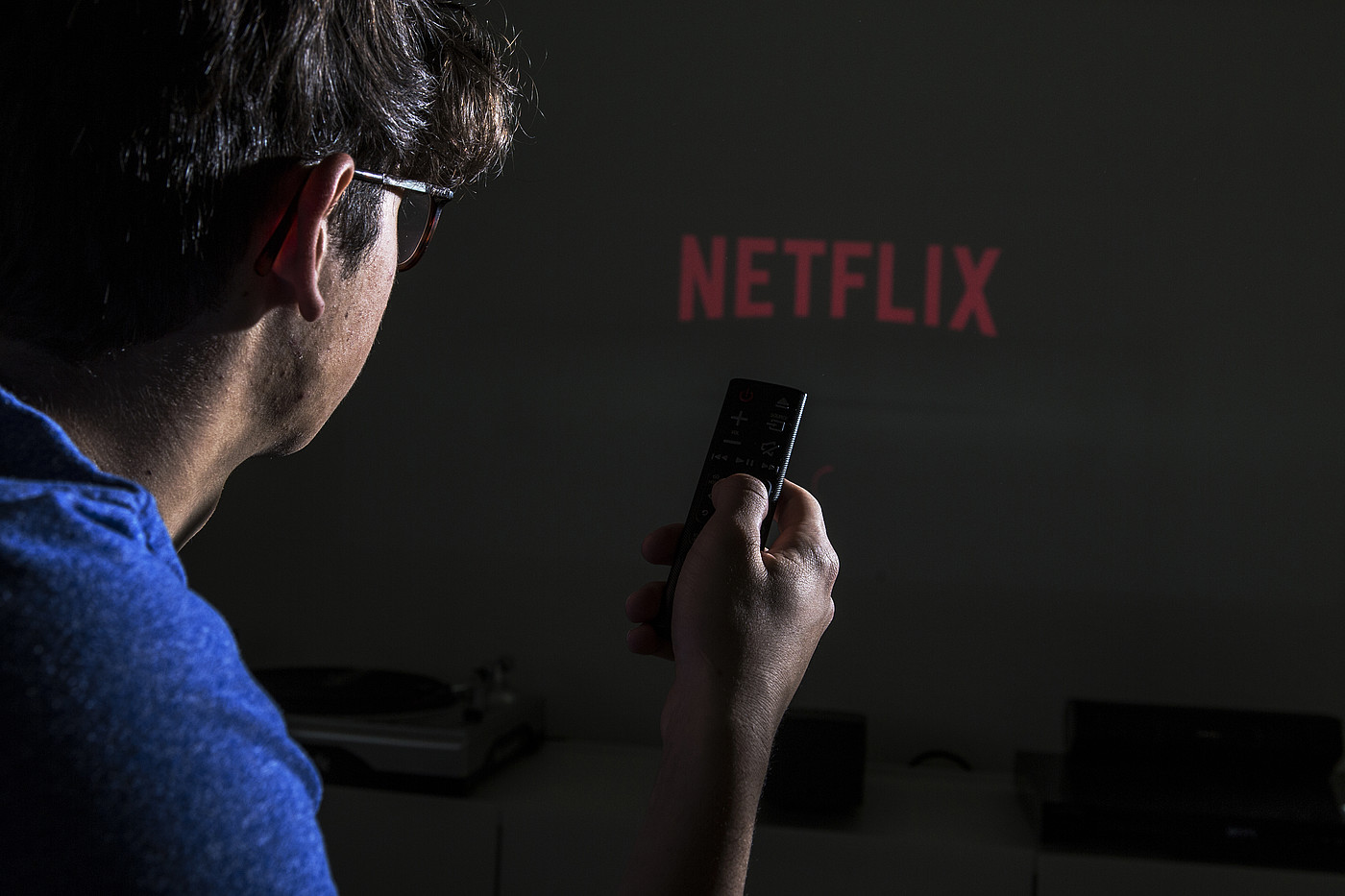 Une personne avec une télécommande à la main. En arrière-plan, vous pouvez voir le logo de Netflix.
