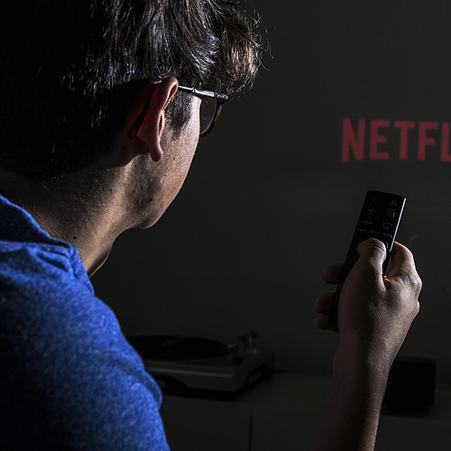 Une personne avec une télécommande à la main. En arrière-plan, vous pouvez voir le logo de Netflix.