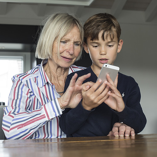 Une femme âgée montre à un jeune garçon comment utiliser un smartphone.