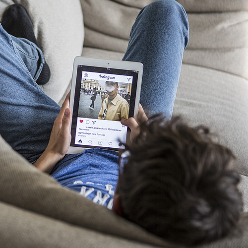 Un adolescent allongé sur le canapé, Instagram ouvert sur sa tablette.