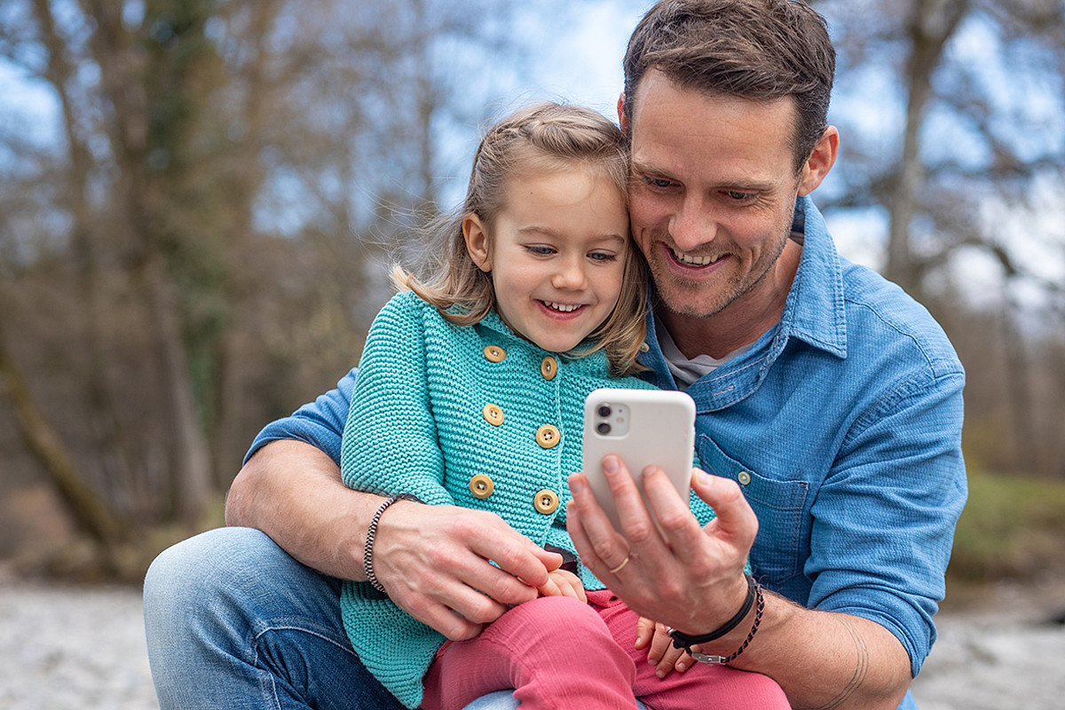Un père avec un enfant sur ses genoux regardant ensemble un smartphone.