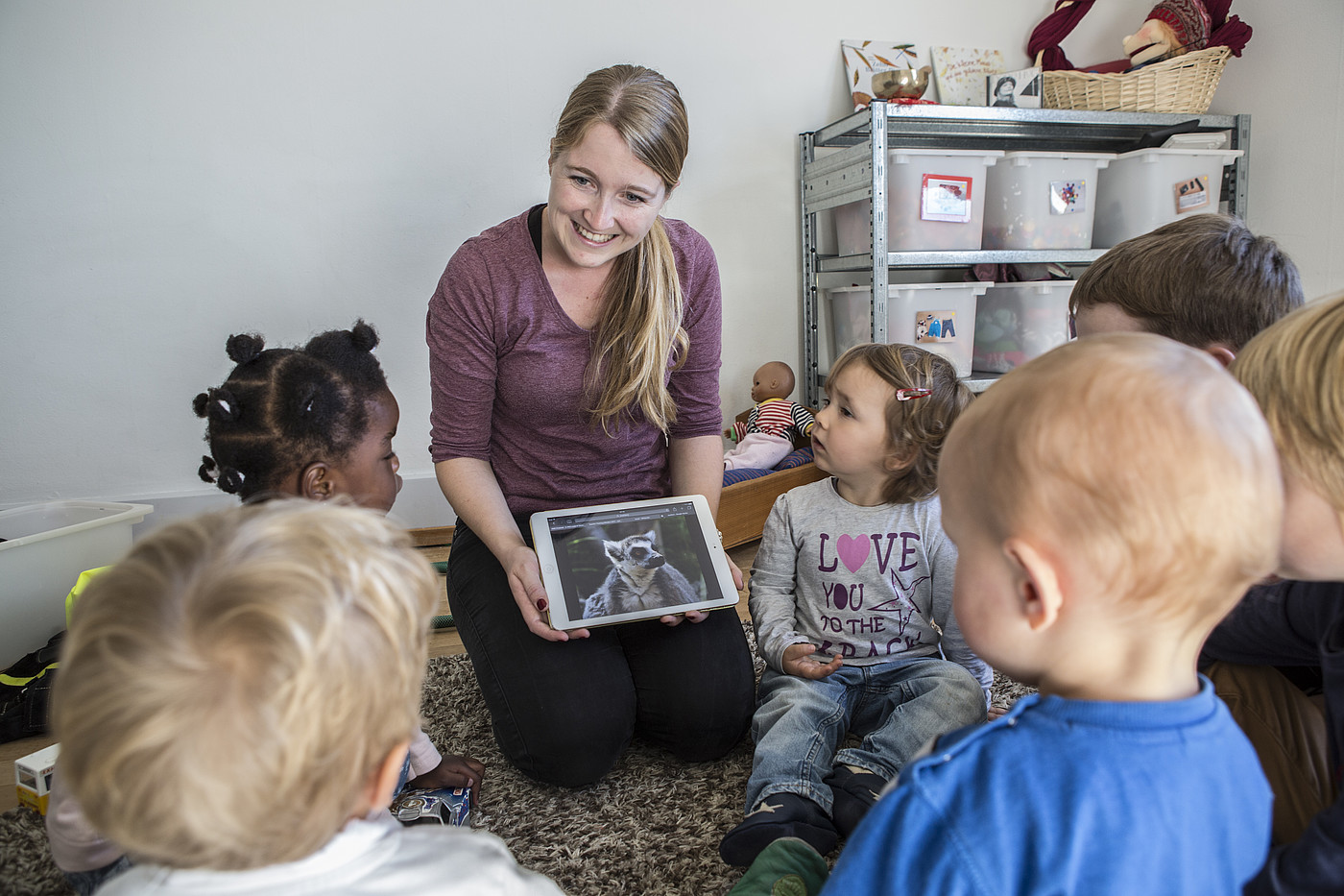 Une assistante maternelle racontant quelque chose aux enfants avec la tablette.