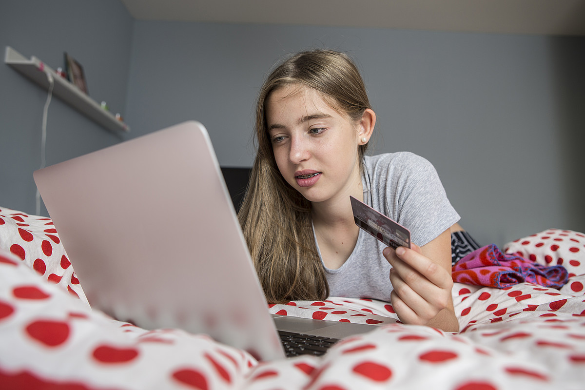 [Translate to Deutsch:] Eine Jugendliche liegt mit dem Laptop auf dem Bett und kauft sich etwas mit der Kreditkarte.