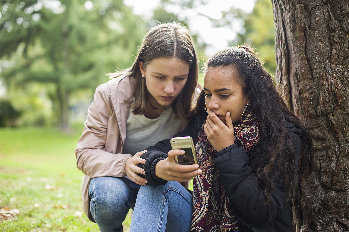 Deux adolescents à l'extérieur regardent un téléphone portable d'un air choqué.