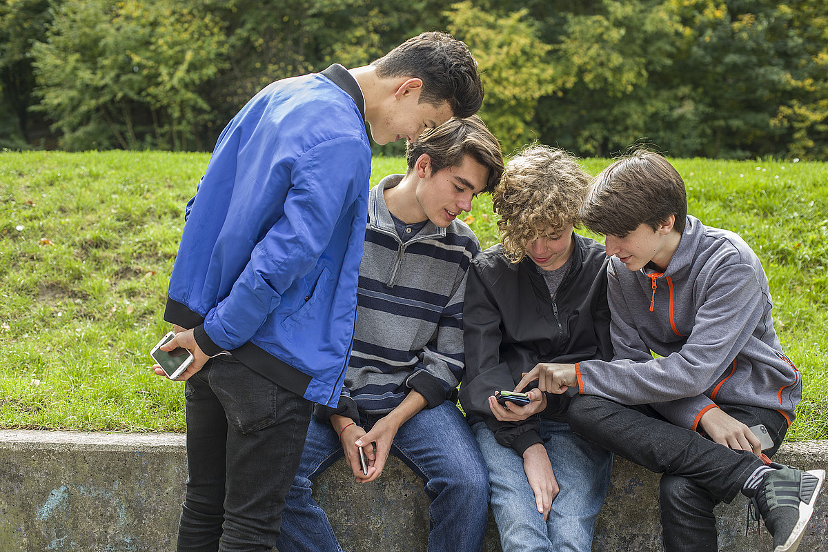 Quatre adolescents à l'extérieur sur leurs téléphones portables.
