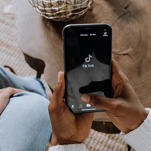 Deux personnes sont assises l'une à côté de l'autre, l'une d'elles tient un smartphone avec le logo TikTok dessus