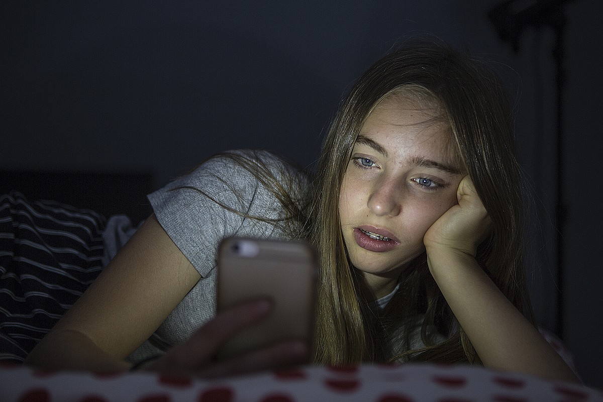 Une adolescente est allongée sur son téléphone portable dans le noir. 