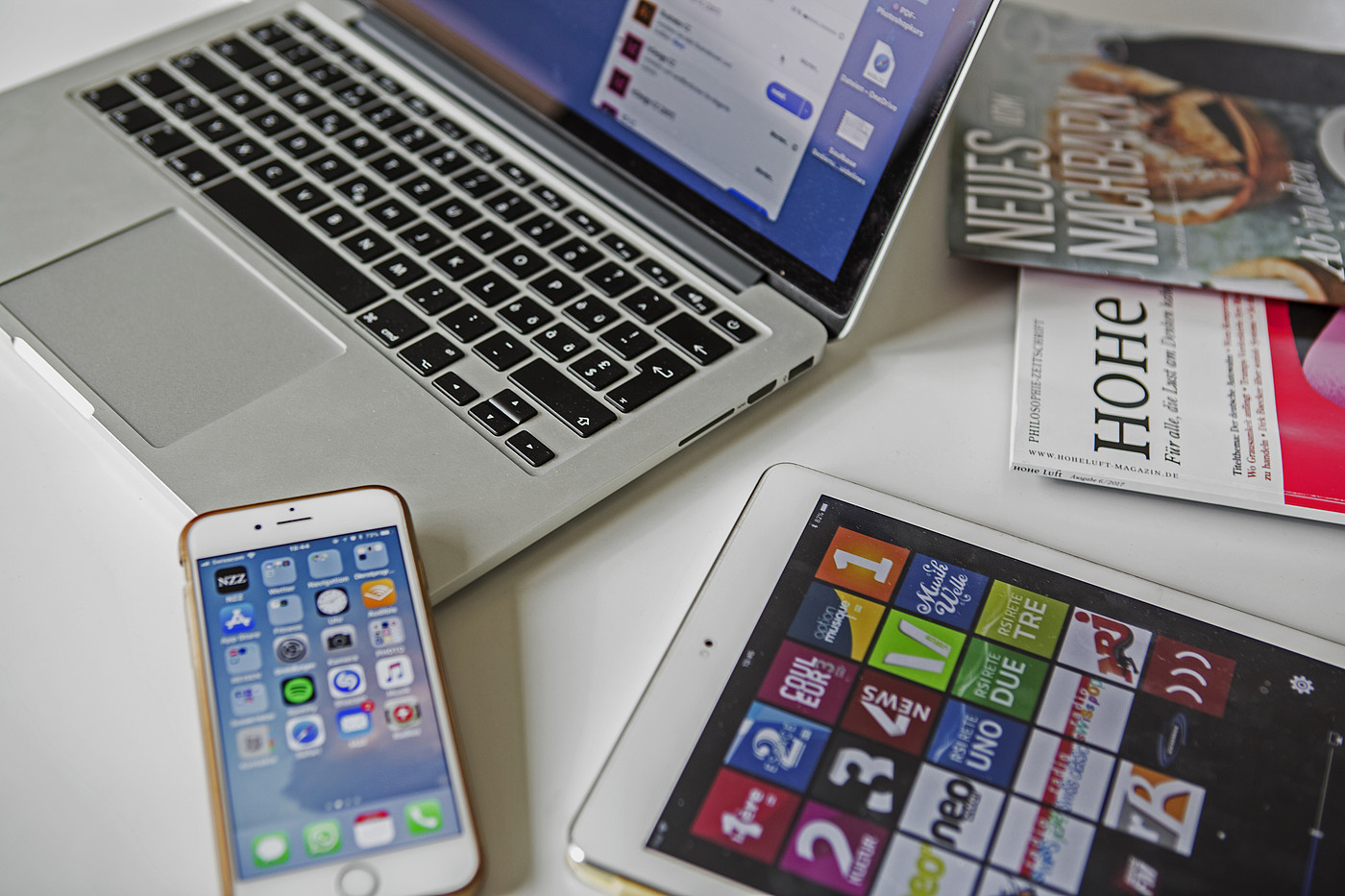 Un ordinateur portable, un smartphone, une tablette et des magazines posés sur une table.