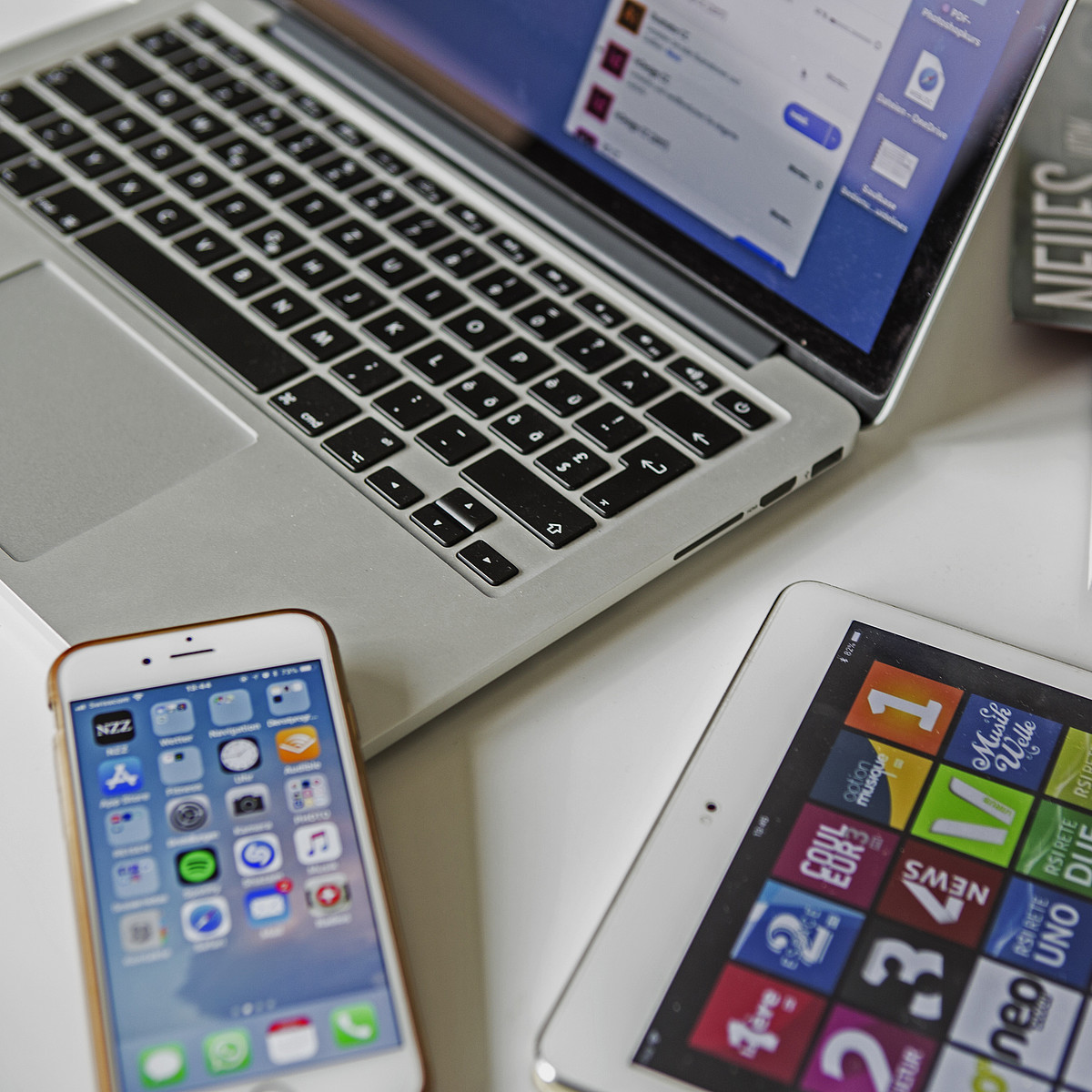 Un ordinateur portable, un smartphone, une tablette et des magazines posés sur une table.