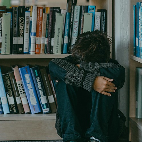 Un garçon est assis recroquevillé sur le sol de la bibliothèque. 