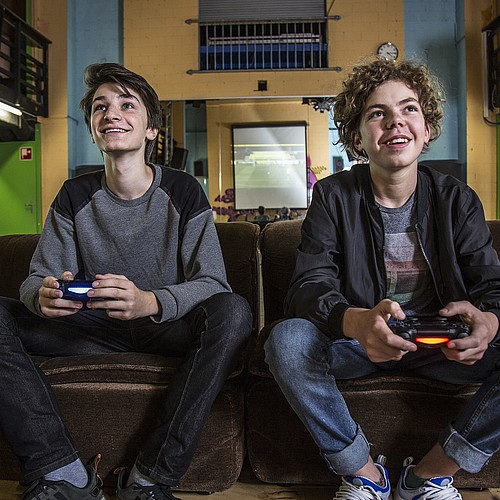 Deux adolescents assis sur un canapé dans un club de jeunes jouent ensemble à un jeu vidéo.