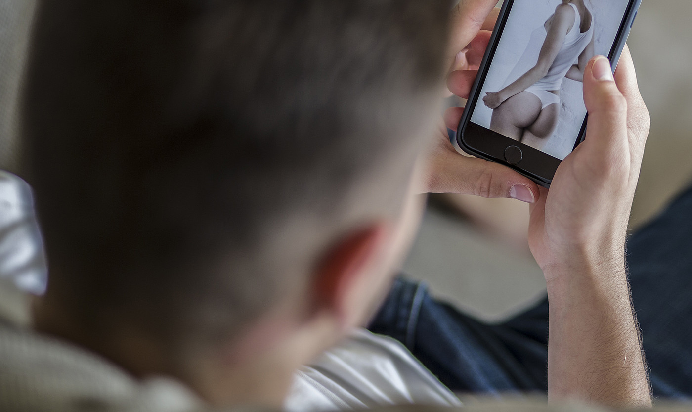 Un jeune homme regarde une photo de femme à moitié nue sur son téléphone portable. 