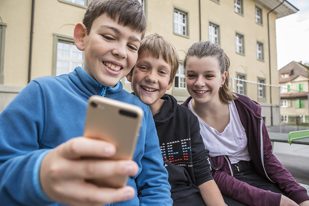 Trois enfants regardant ensemble un smartphone.